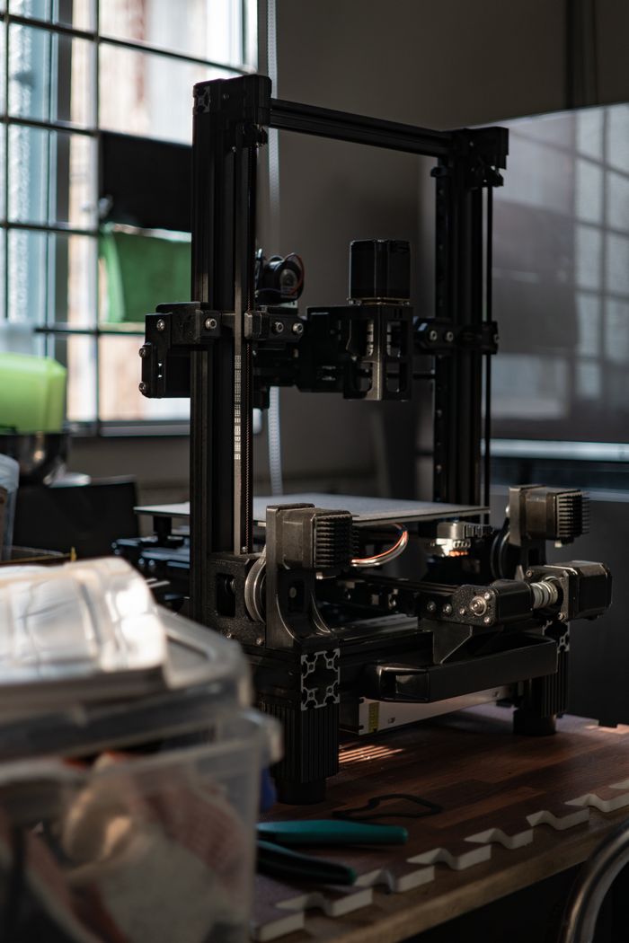 A detailed view of a 3D printer in a workshop with ambient light.
