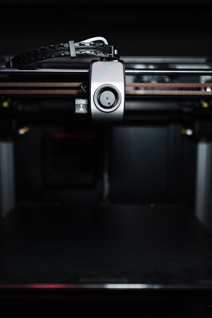 who-we-are Close-up of a high-precision industrial 3D printer nozzle in a dark setting, showcasing advanced technology.