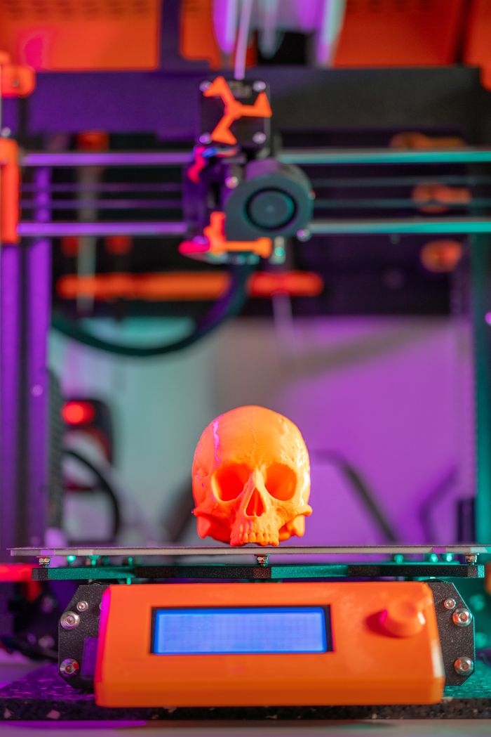 services-01 A vibrant 3D printed skull displayed on a printer in a colorful workshop setting.