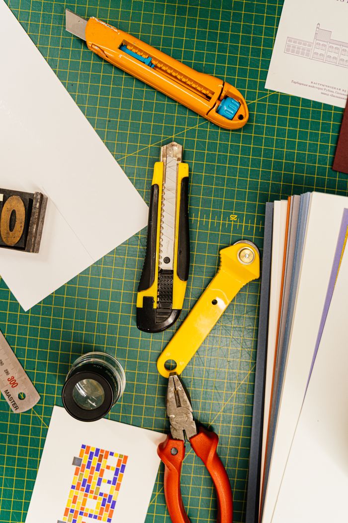 Top view of various cutting tools on a green grid mat surrounded by papers, ideal for creative projects.